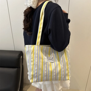 Chic striped canvas tote bag in yellow and purple shown worn on the shoulder