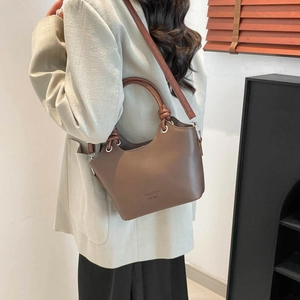 Chic brown bucket bag with top handle and crossbody strap styled in minimalist interior