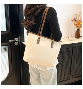 Detail of a large cream tote bag with brown straps worn on a shoulder for daily commute