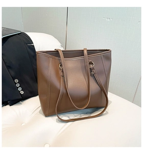 Detail shot of a brown leather tote bag with long slim handles on a white textured surface