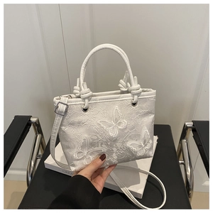 Detailed view of a white lace bucket bag with 3D butterfly appliques and knotted handle