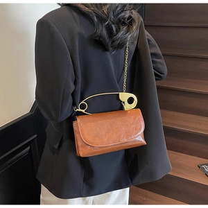 Detail of dark brown retro square bag with gold safety pin handle on black blazer