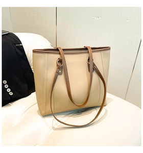 Detail view of a beige minimalist tote bag with dark brown handles on a white leather bench