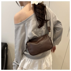 Brown leather pillow bag with a patterned wide strap worn by a model in casual style