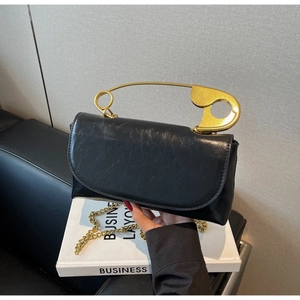 Detail of black glossy handbag featuring a unique gold safety pin handle and chain strap