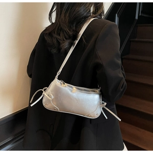 Detail of silver metallic underarm bag with woven bow ties and metal studs on shoulder
