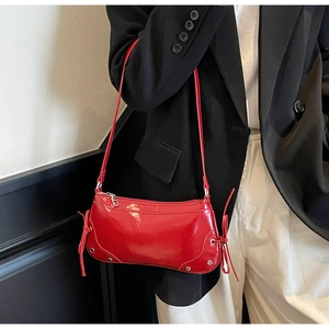 Detail view of red glossy baguette bag with silver studs and side drawstring detail
