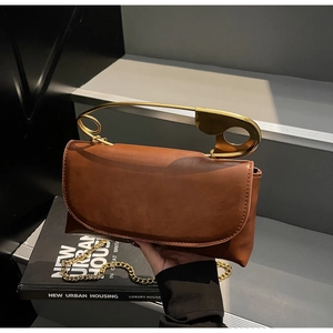 Detail of creative golden oversized pin handle on a brown leather handbag with chain strap