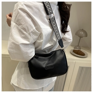 Detail of black crossbody pillow bag with wide geometric strap and gold-tone metal clips