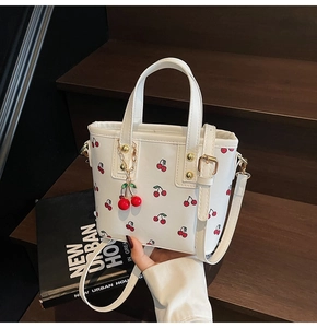Detail of white mini bucket bag with red cherry prints and decorative charm pendant