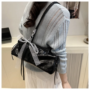 Detail of black glossy barrel bag featuring a white lace bow and long tassel drawstrings