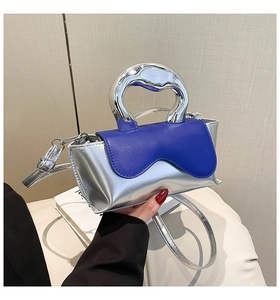 Detail of silver metallic handbag with blue wavy flap held by hand in soft light
