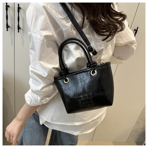 Detail of black glossy bucket bag featuring embossed MEIGE SNUR GOOD text and gold hardware