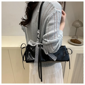 Close-up of black glossy baguette bag with white lace trim and ribbon bow on model