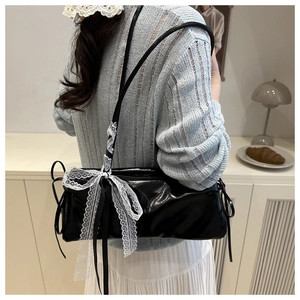 Detail of black glossy baguette bag with white lace bows worn by a model in soft lighting