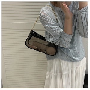 Detail of black transparent handbag with gold chain strap worn over a knit top