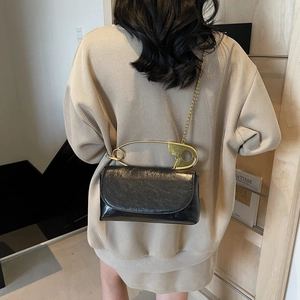 Minimalist black glossy leather crossbody bag with iconic gold safety pin handle handle