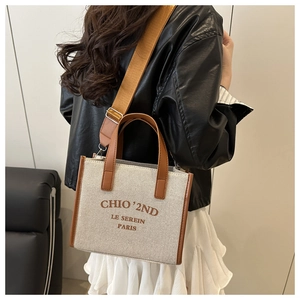 Detail of canvas tote bag with brown leather trim shown on a model's shoulder