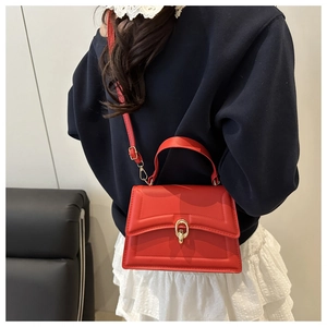 Detail of red crossbody bag with gold ring buckle and quilted texture on a model