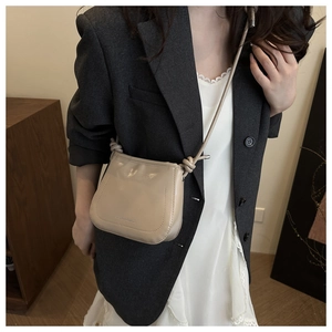 Detail of light beige bucket bag with glossy finish and stylish knot shoulder strap