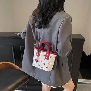 Fashionable white bucket bag with red cherry print and adjustable strap shown on model