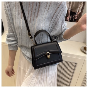 Detail of a chic black crossbody bag with gold twist lock and textured surface
