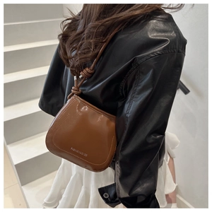 Close-up of brown patent leather saddle bag with unique knot detail on the shoulder strap