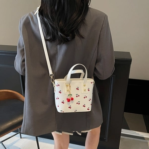 Mini white bucket bag with cherry print, featuring dual handles and a red cherry charm