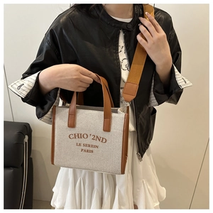 Close-up of cream canvas tote bag with brown leather trim and wide textile strap