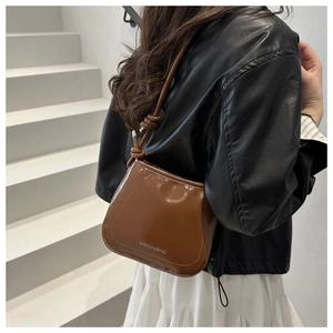 Detail of coffee brown glossy patent leather bucket bag with knotted shoulder strap decor