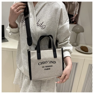 Detail of cream canvas tote bag featuring black wide shoulder strap and brand logo