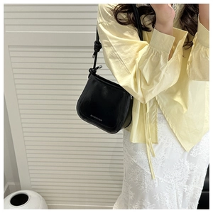 Detail of black semi-circle crossbody bag with silver text logo and knot strap accents