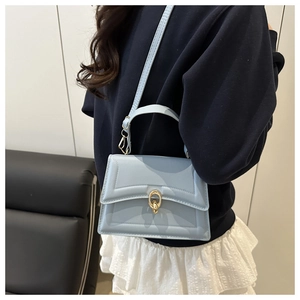 Detail of light blue square bag featuring gold ring clasp and textured line patterns