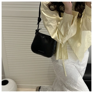Detail of a black leather hobo bag with a knotted strap and white logo text on a model