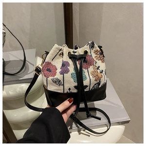 Detail of canvas bucket bag with floral embroidery, leather drawstring, and adjustable strap