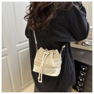 Detail of woven straw bucket bag featuring white leather base and drawstring closure