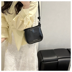 Detail of black glossy bucket bag featuring knot shoulder strap and white logo print