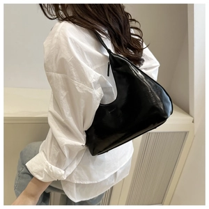 Close-up of black glossy crescent bag on shoulder with casual white shirt and jeans