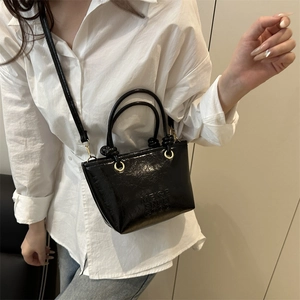 Sleek black textured bucket bag with top handles and shoulder strap shown on a model