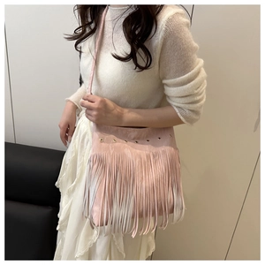 Detailed side view of pink faux suede crossbody bag with decorative fringe and metal eyelets
