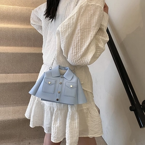 Blue shirt-shaped leather crossbody bag with metal chain strap worn on a white dress