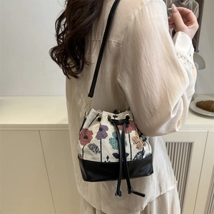 Floral canvas drawstring bucket bag with black leather straps worn by a model
