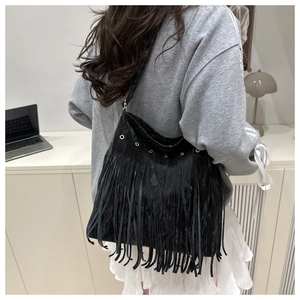 Detail of black matte leather shoulder bag with long fringes and silver eyelets on model