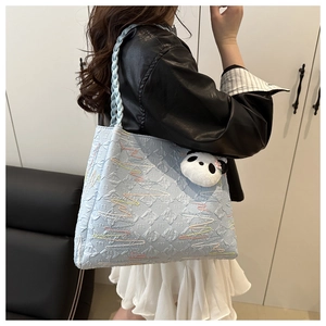 Detail of light blue tote bag with colorful wave embroidery and a cute panda pendant