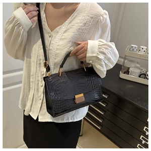 Detail of black crocodile texture handbag with gold metal hardware on model in cozy room