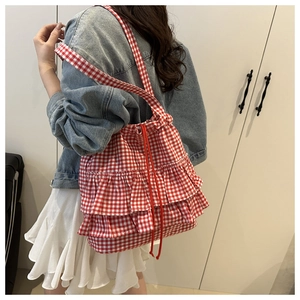 Detail of red gingham ruffle tote bag with drawstring closure worn on shoulder