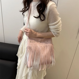 Pink faux suede crossbody bag featuring gold eyelets and long decorative fringe details