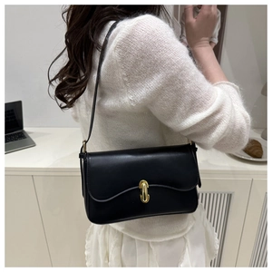 Detail of minimalist black leather underarm bag with gold buckle on a white sweater