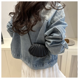 Close-up of a black shell-shaped mini crossbody bag with vertical texture worn on shoulder