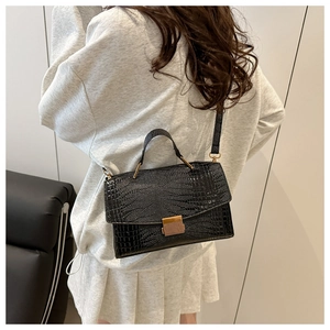 Détail du sac bandoulière noir texture crocodile avec boucle dorée sur un mannequin